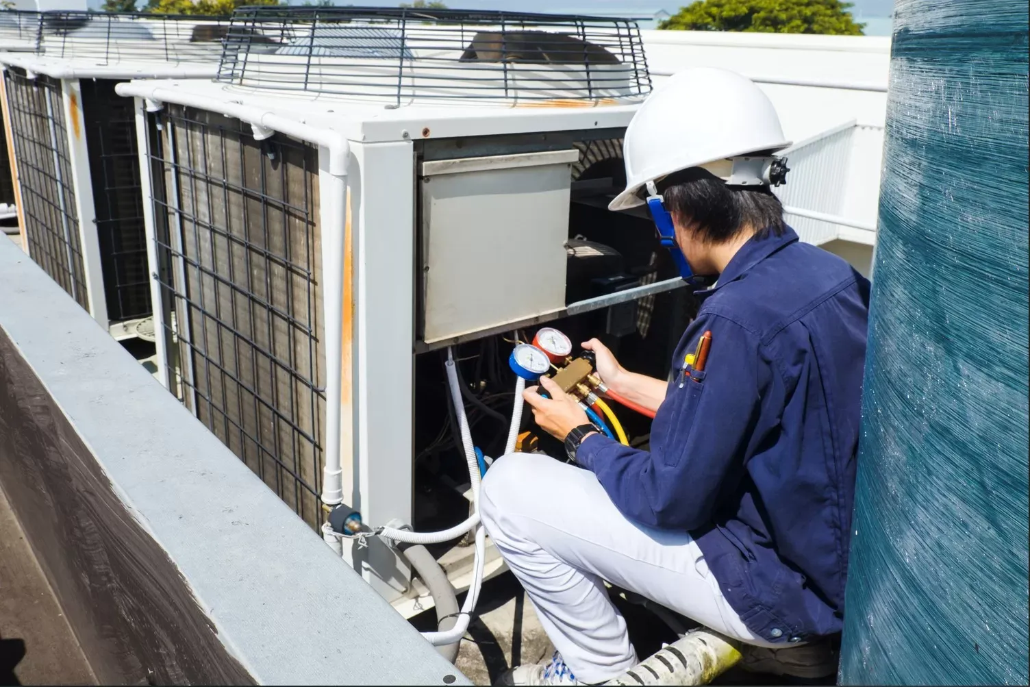 HVAC technician using refrigerant gauges on a rooftop AC unit during commercial HVAC service in Billerica MA